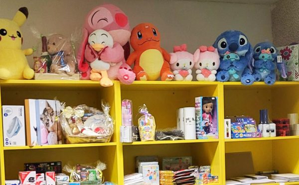 Ein leuchtend gelbes Regal, auf dem oben bunte Plüschtiere stehen, darunter Figuren wie Pikachu und Hello Kitty. Darunter befinden sich Geschenkkörbe, Puppen und Puzzles